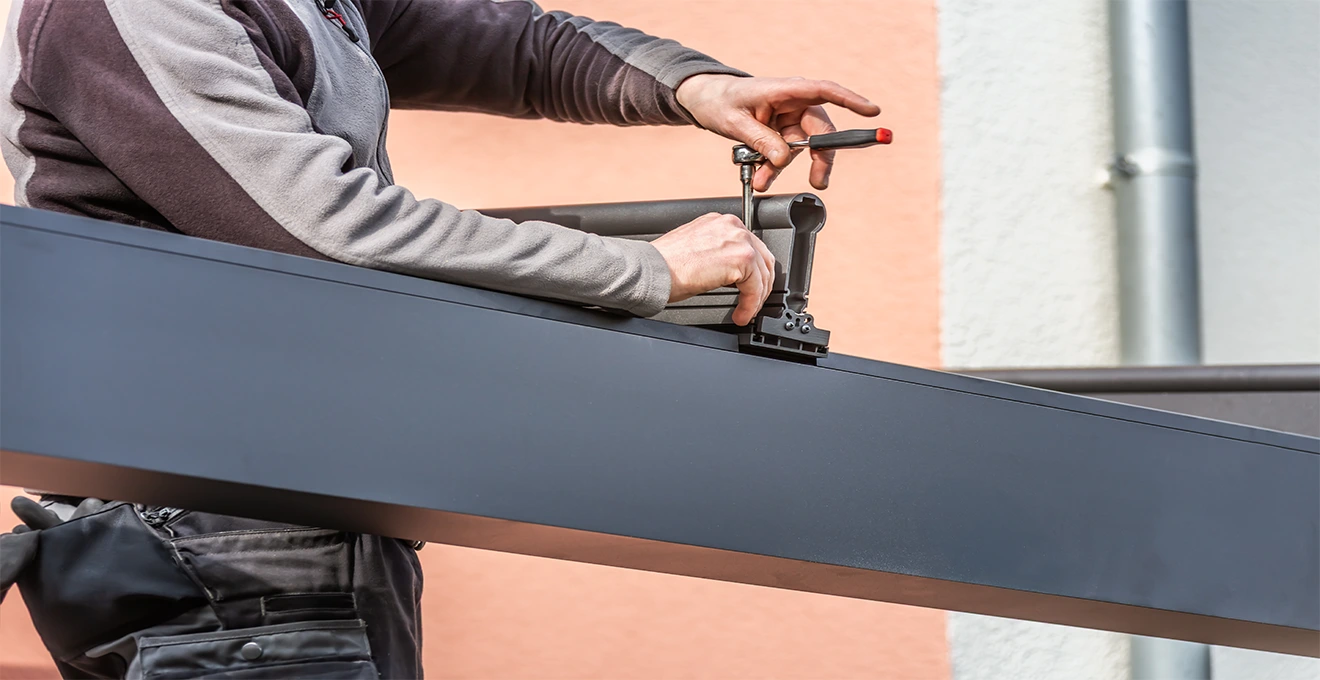Installateur professionnel vérifiant l'orientation d'une pergola bioclimatique en cours d'installation avec un niveau numérique
